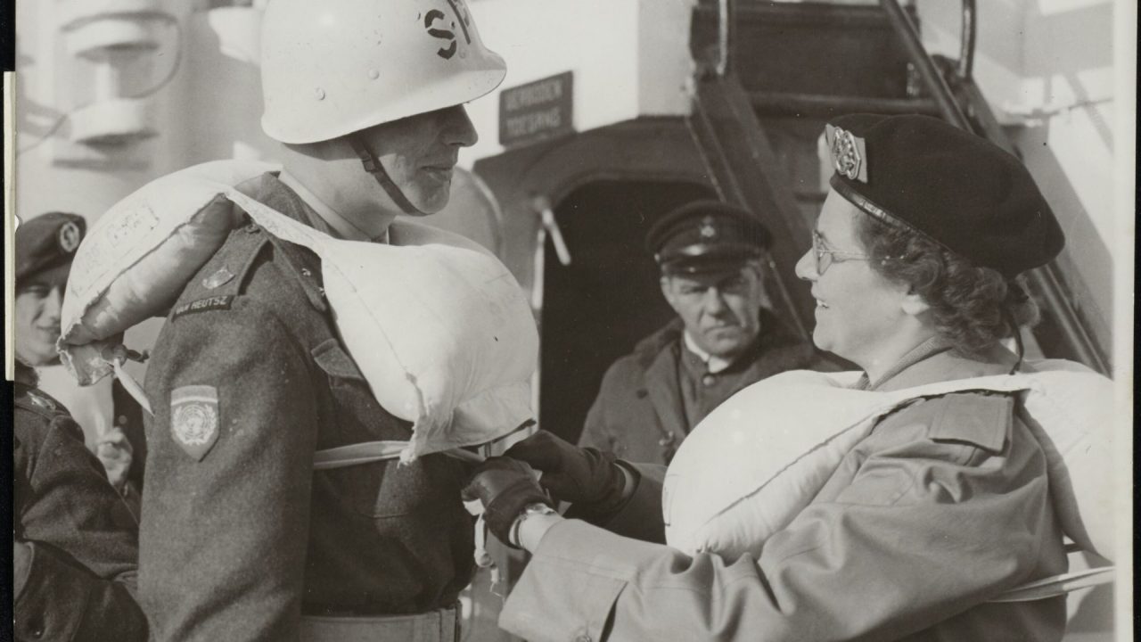 Luitenant-verpleegster helpt met het omgorden van de reddingsgordels bij een militaire vrijwilliger vlak voor vertrek naar Korea (1950)